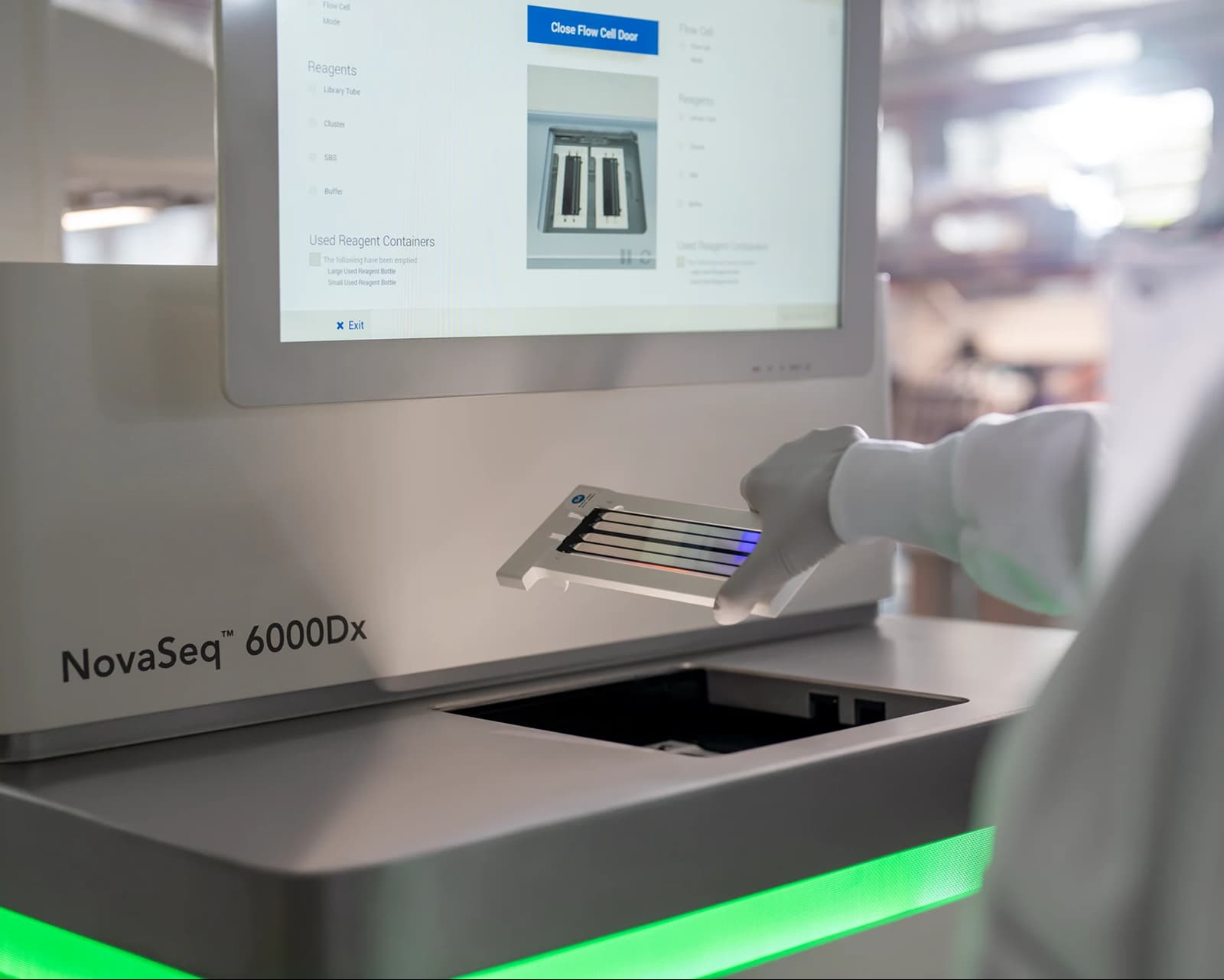 Close up, back view of a scientist inserting a flow cell in the flow cell compartment of a NovaSeq 6000dx; partial view of flow cell touch screen and green status bar visible.