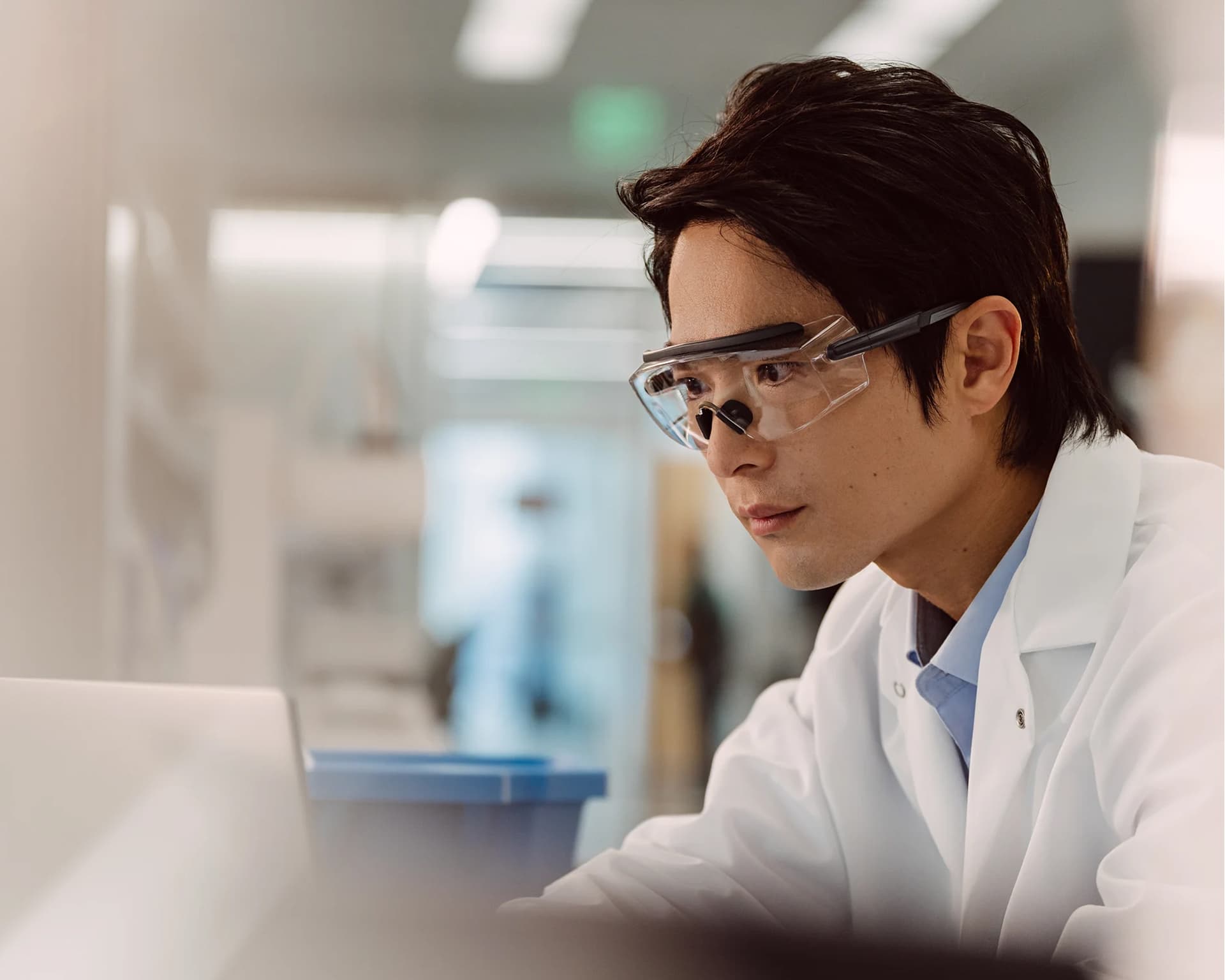 Male scientist analyzing a monitor on a laptop, not visible, in a lab setting.