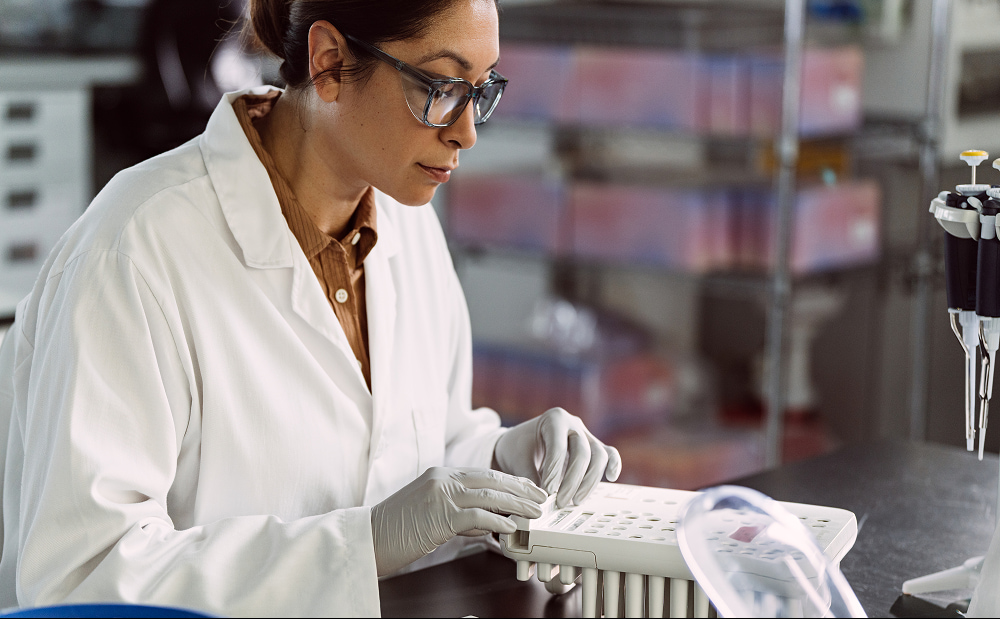 Female scientist inserting a 8 flow cell lane library tube strip into into sequencing reagent cartridge on lab bench with other consumables, single pipettes, and library tubes in the foreground.